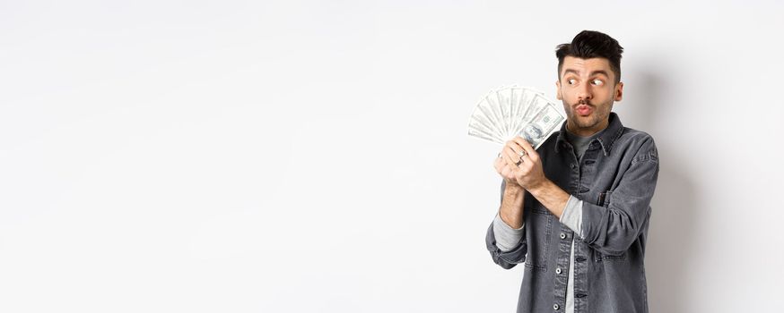 Excited man hugging and kissing dollar bills, holding money and rejoicing, standing on white background.