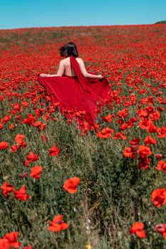 Young woman stands with her back in a long red dress and hat, posing on a large field of red poppies.