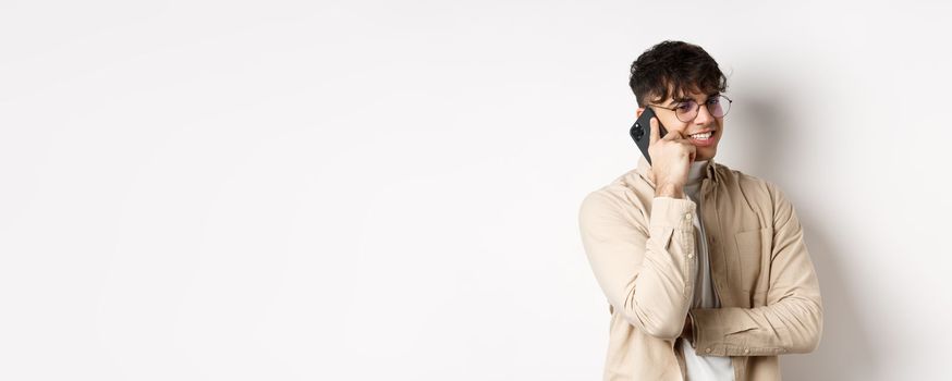 Real people concept. Handsome modern man talking on mobile phone, look aside and holding smartphone near ear, standing on white background.