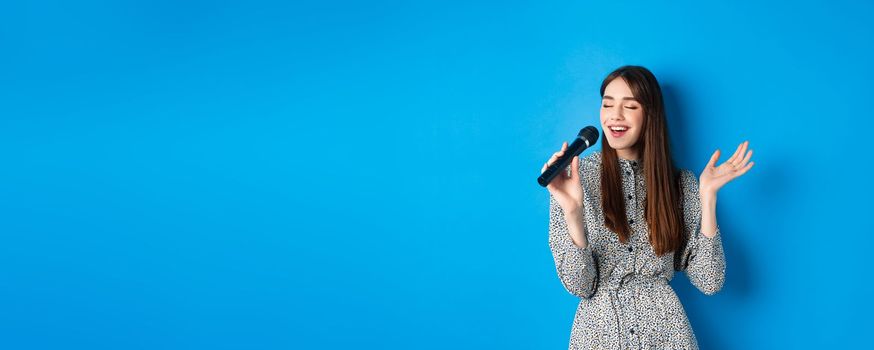 Beautiful candid girl singing in microphone, close eyes and smile carefree, sing at karaoke. Leisure and hobbies concept.