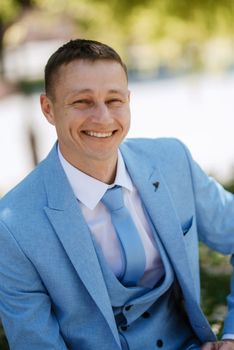 portrait of the groom's boyfriend in a blue suit smiling while sitting on a bench