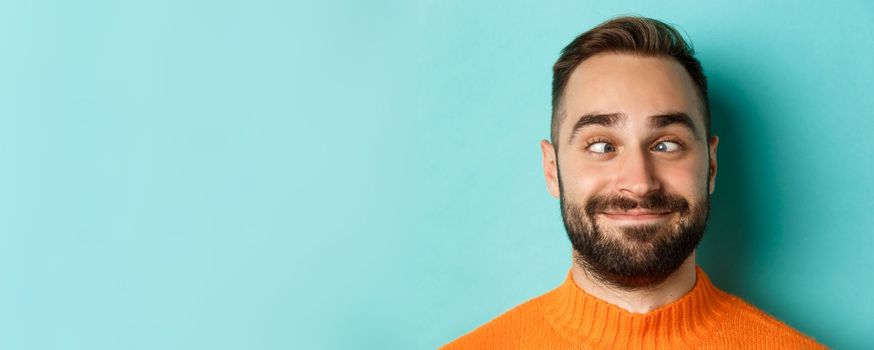 Headshot of funny caucasian man making faces, squinting and smiling silly, standing over light blue background.