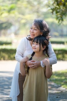 Asian Grandmother and Granddaughter hug together outdoor park. Hobbies and leisure, lifestyle, family life, happiness moment concept.