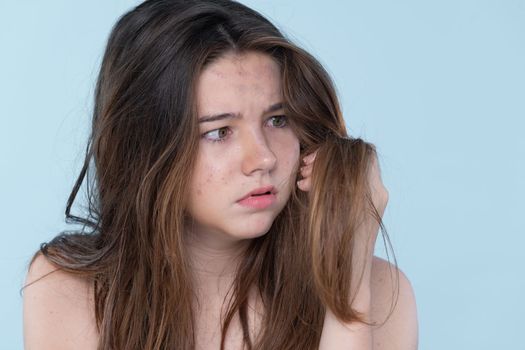 Beautiful girl feel sad, worry about her damaged hair with isolated background. Concept of dry lifeless hair. Young charming girl hold her tangled hair and look at it with worried expression.