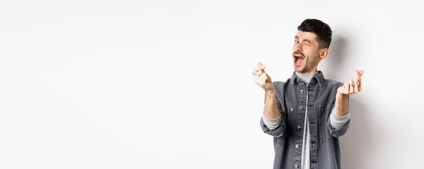 Funny guy winking and showing hand hearts sign, feeling romantic and happy, standing on white background.