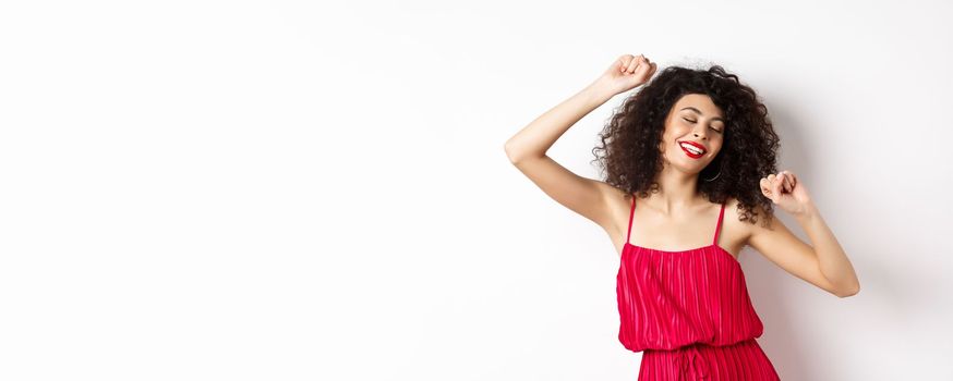 Happy elegant woman in red dress dancing on white studio background.