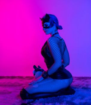 sexy girl in costume and mask bdsm games in neon light with empty background