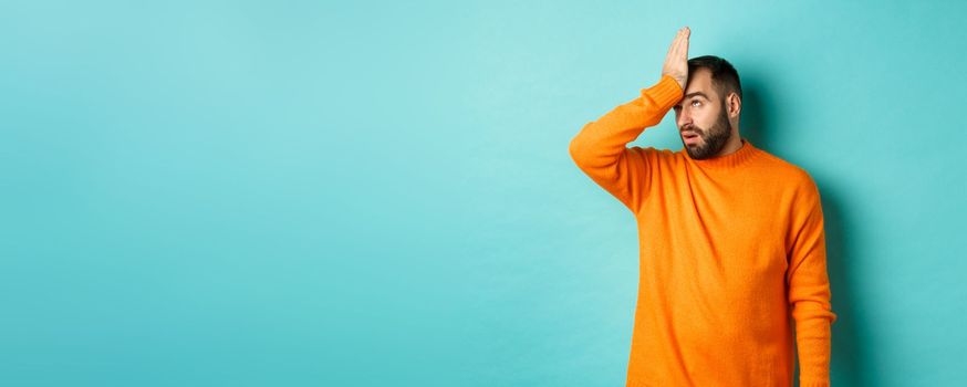 Annoyed man roll eyes and making facepalm, standing over turquoise background.