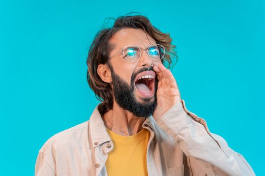 Young man shouting loud calling attention isolated on blue studio background. High quality photo