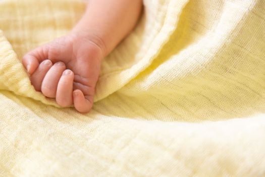 Newborn premature baby hand on pastel yellow soft muslin blanket. Copy space, space for text