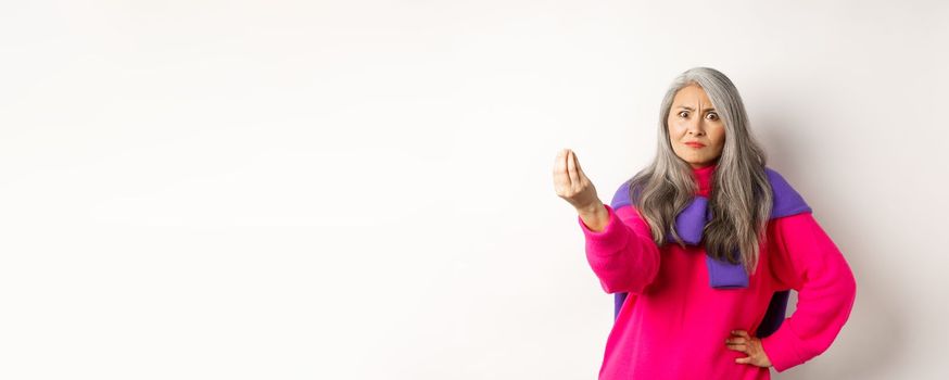 Funny asian woman staring angry and confused, shaking fingers, standing grumpy against white background. Copy space