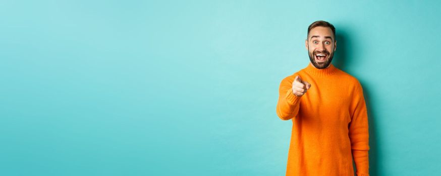 Surprised man stare happy and pointing at camera, recognize someone, excited about seeing something, standing over light blue background.