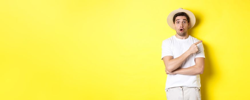 Surprised man in straw hat pointing finger right, showing promo banner, standing over yellow background. Copy space