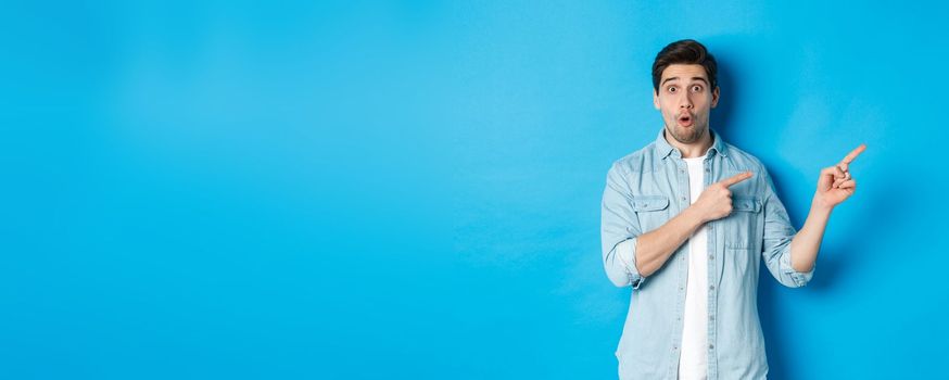 Portrait of surprised bearded guy in casual outfit pointing fingers right, showing amazing promo offer, standing over blue background.