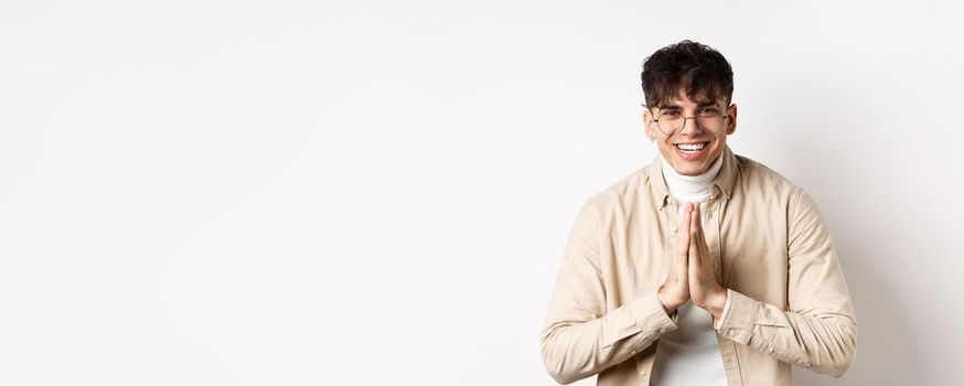 Handsome caucasian man say thank you, bowing with namaste gesture, looking grateful and smiling at camera, standing on white background.