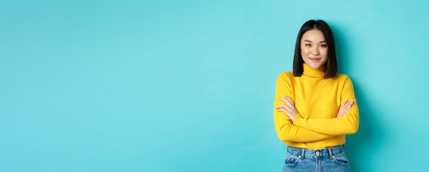 Attractive asian woman with short dark hair, cross arms on chest and smiling confident, standing over blue background.