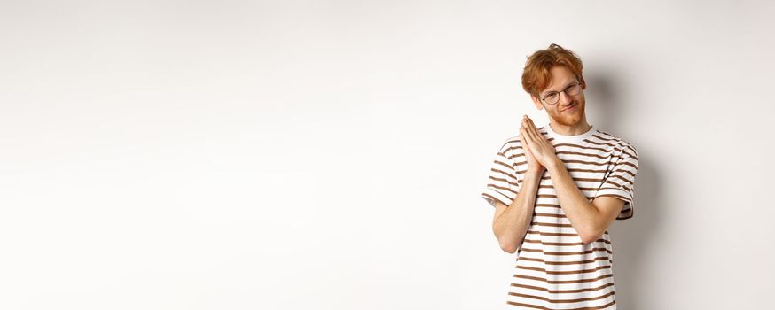 Cunning redhead man having plan, rubbing palms and looking devious at camera, smirk and squint sly, standing over white background.