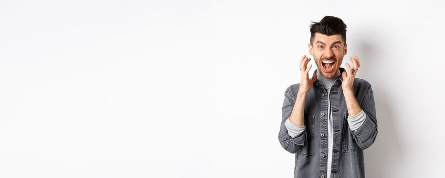 Angry man screaming distressed, losing temper and shouting frustrated, staring at something bad, standing on white background.