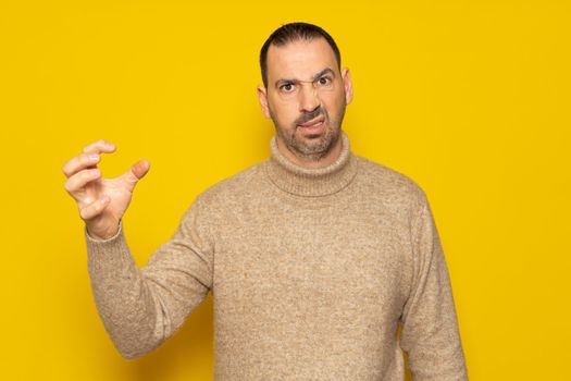Bearded hispanic man wearing turtleneck over isolated yellow background doing cat claw gesture because of extreme anger having, aggressive expression