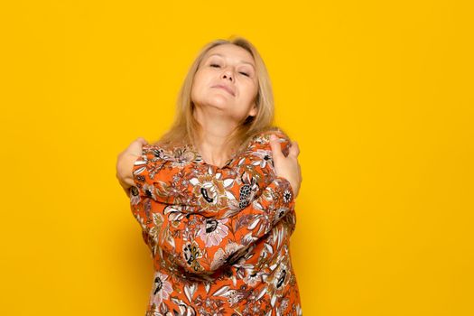 Close-up photo of a charming woman wearing a dress while smiling and hugging herself, isolated over yellow background