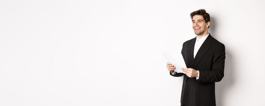 Image of handsome businessman in suit, holding documents and smiling, standing against white background.