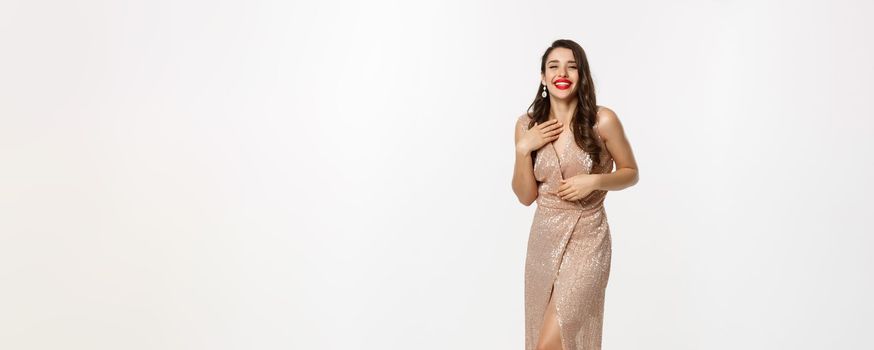 Party and celebration concept. Full-length of beautiful woman in elegant dress standing near Christmas gifts, laughing happy, standing over white background.