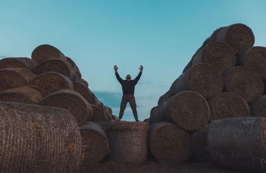 man raising his hands stands on a pyramid of hay