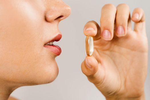 Omega 3 pill of fish fat oil near lips close-up. BADS capsule of biologically active dietary supplements. Vitamin D for building and maintaining healthy bones