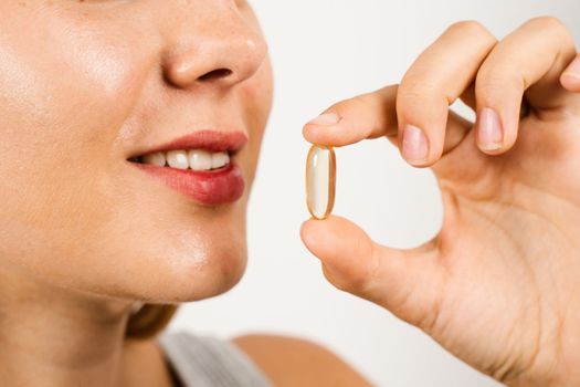 Girl is taking BADS capsule of Omega-3 biologically active dietary supplements close-up. Vitamin D for building and maintaining healthy bones