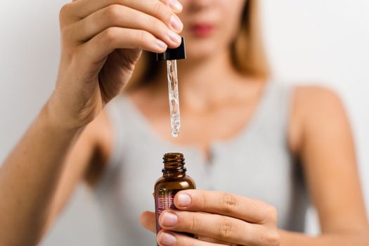 Face serum pipette close-up in hands of attractive girl on white background. Girl applies face serum to her face with pipette on white background