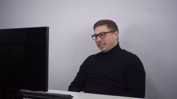 A young man looks at a computer monitor and laughs emotionally. An IT specialist in glasses sits in the office and watches a movie. 4k