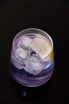 refreshing drink gin and tonic of purple color in a transparent glass on a black background. High quality photo