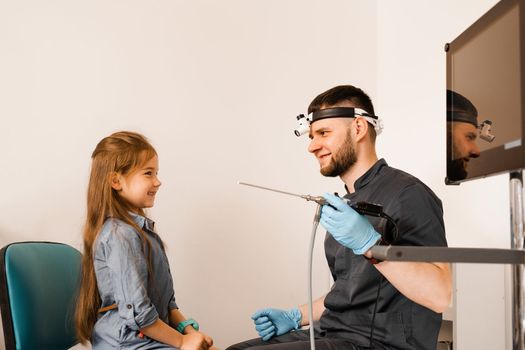 ENT doctor otolaryngologist with headlight showing to child endoscope for rhinoscopy and otoscopy. Nose and ears endoscopy of child