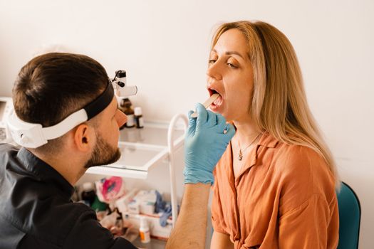 Oropharyngoscopy procedure. Otolaryngologist examines woman throat with spatula. Consultation with laryngologist