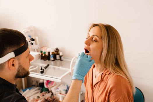 Oropharyngoscopy procedure. Otolaryngologist examines woman throat with spatula. Consultation with laryngologist