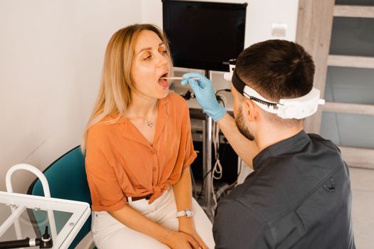 Oropharyngoscopy procedure. Otolaryngologist examines woman throat with spatula. Consultation with laryngologist