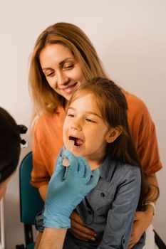 Oropharyngoscopy procedure for child. Otolaryngologist examines child throat with spatula. Family consultation with laryngologist