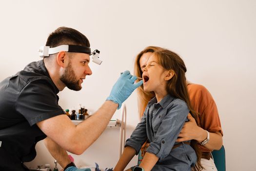 Oropharyngoscopy procedure for child. Otolaryngologist examines child throat with spatula. Family consultation with laryngologist