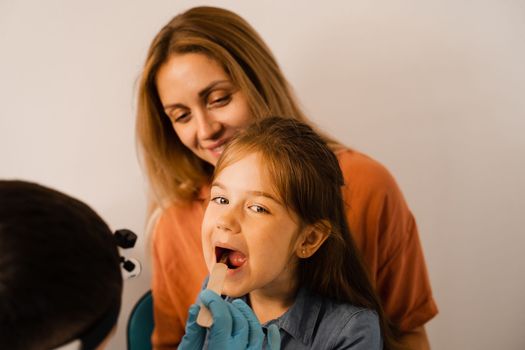 Oropharyngoscopy procedure for child. Otolaryngologist examines child throat with spatula. Family consultation with laryngologist