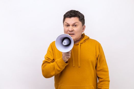 Optimistic middle aged man screaming in megaphone, announcing important information with positive, looking at camera, wearing urban style hoodie. Indoor studio shot isolated on white background.