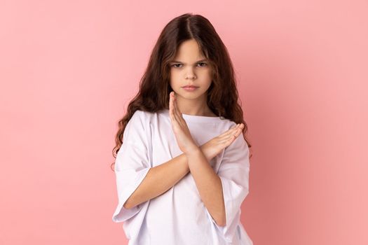 No way, absolutely not. Portrait of little girl wearing white T-shirt showing x sign with crossed hands, meaning stop, this is the end. Indoor studio shot isolated on pink background.