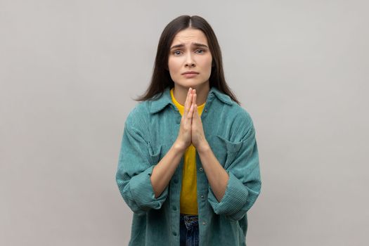 Please, I'm begging. Desperate woman keeping arms in prayer gesture and asking forgiveness, feeling sorry for mistake, wearing casual style jacket. Indoor studio shot isolated on gray background.