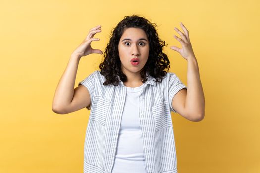 Portrait of exhausted tired woman with dark wavy hair showing mind explosion gesture, feeling unhappy and nervous, lots unnecessary information. Indoor studio shot isolated on yellow background.
