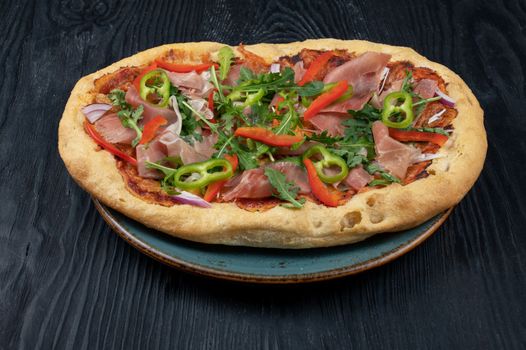 Italian Pizza on plate with jamon slices, pepper and fresh arugula leaves on top