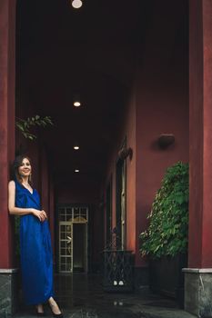 Young woman in blue dress next to exterior of big luxury house.