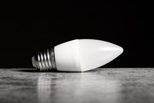 LED energy-saving lamp with E27 screw cap base in form of candle, on black background, copy space.