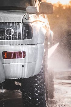 Washing white car at a self-service car wash with a high-pressure water jet after off-road driving, vertical.