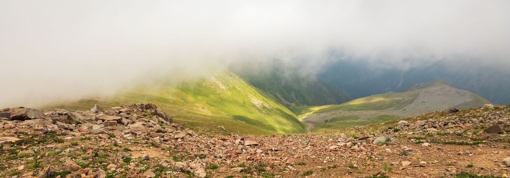 Mysterious minimalist high-altitude picturesque mountain landscape with clouds touching large peaks. Banner format.