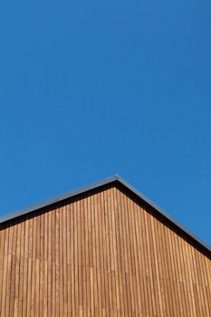 Rooftop with wooden plank gable on new modern home against clear blue sky.