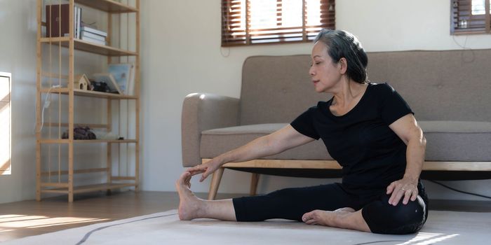 Healthy and happy 60s retired Asian woman in workout clothes practicing yoga in her living room...